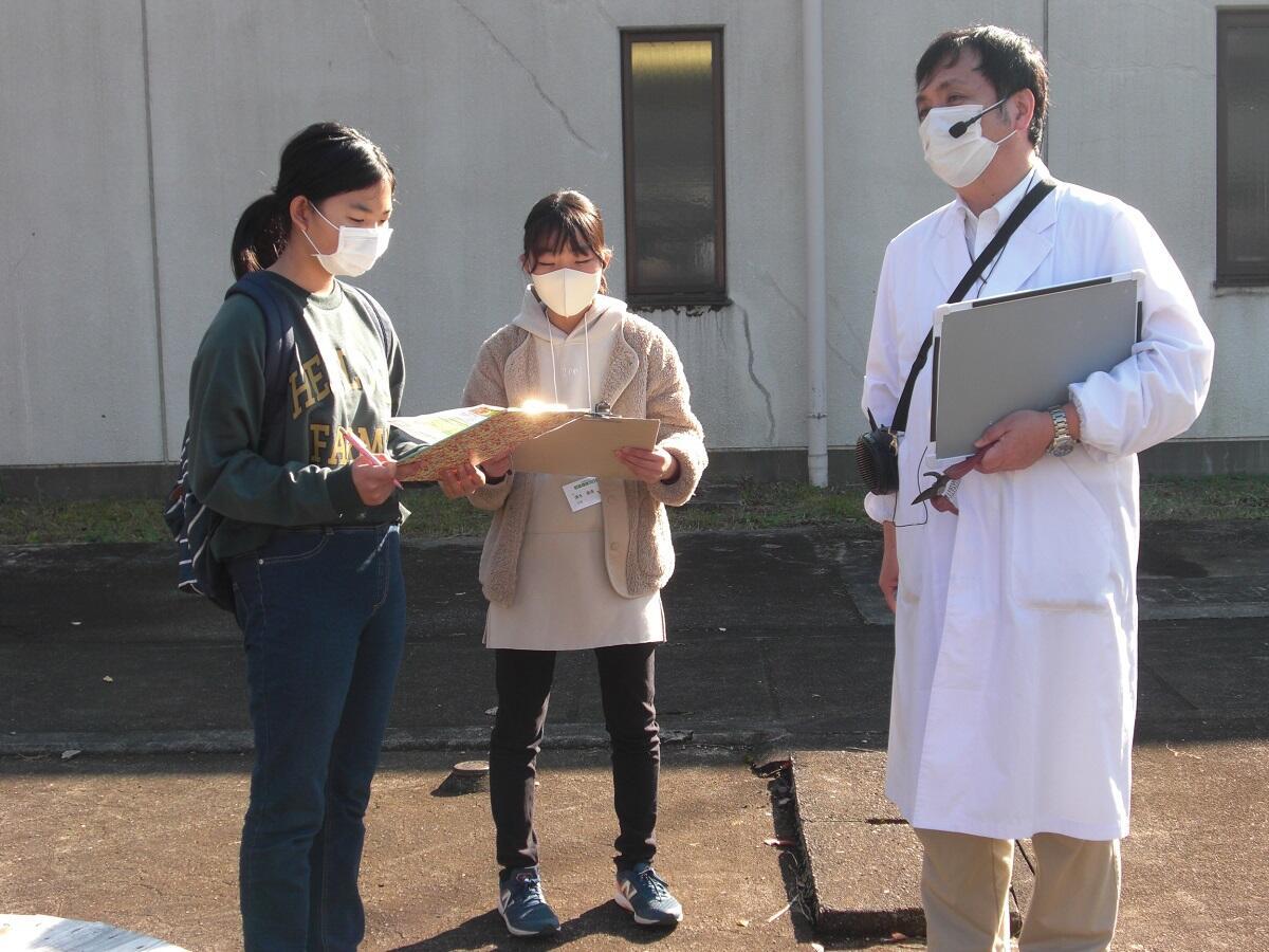 取材中の女子生徒2人、マスク姿、白衣の男性